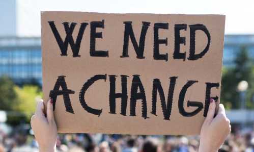 A cardboard protest sign that says we need a change in large black lettering