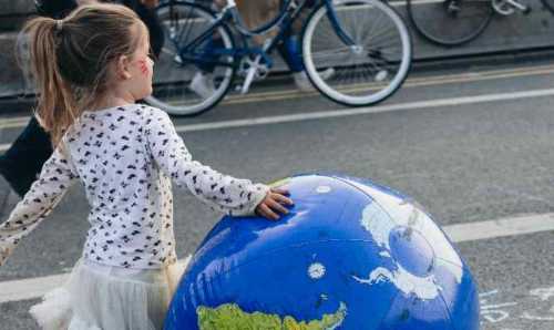 A young girl rolls a blow-up globe down a busy urban street